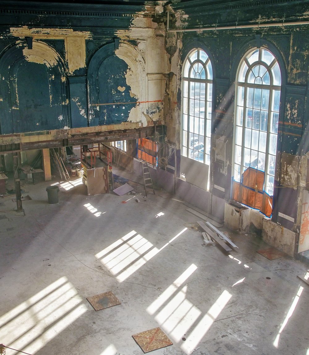 Renovation interior with tall arched windows and distressed blue wall panels.