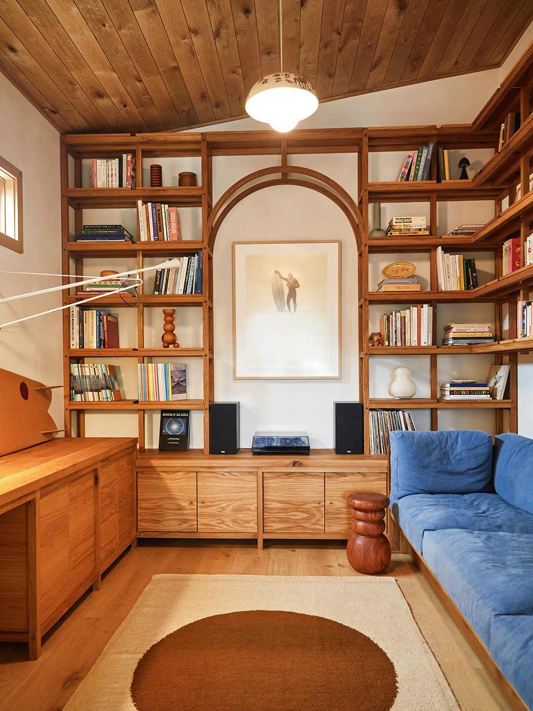 A built-in oak library nook with an arched bookshelf, a blue sofa, and a desk, in a room originally planned as a bedroom.