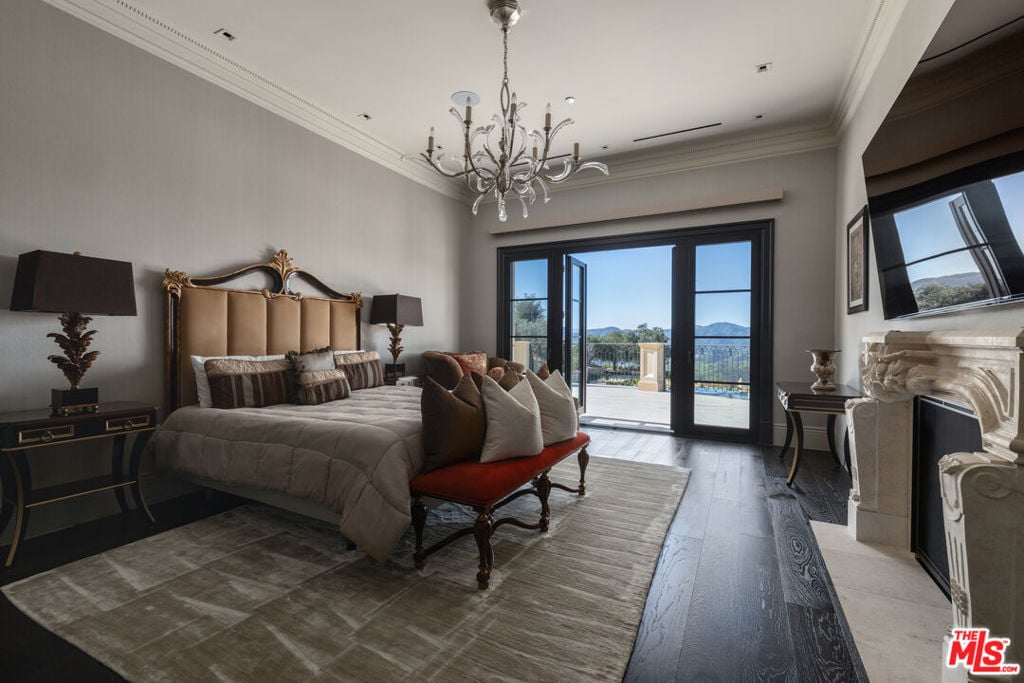 Furnished bedroom with an ornate bed and chandelier, opening onto a terrace with mountain views.