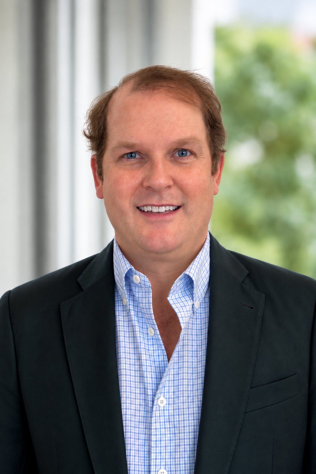 Elliot Poole wearing a dark blazer and blue checked shirt in a professional headshot.