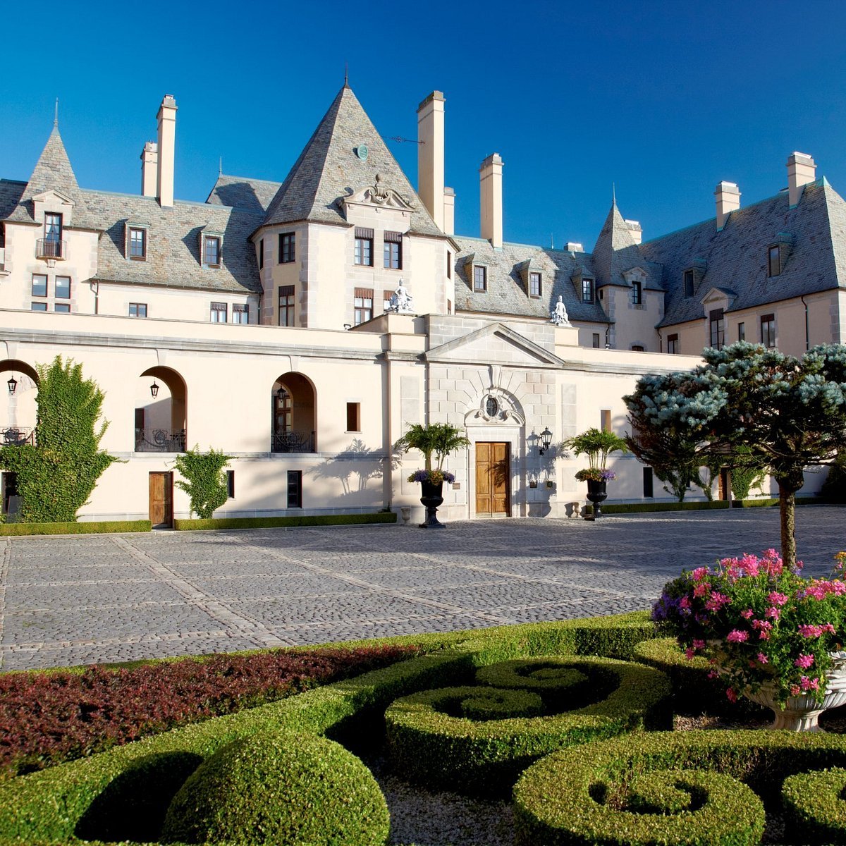 Château-style residence with steep slate roofs, a cobblestone courtyard, and formal clipped-hedge gardens.