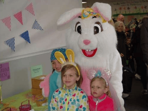 Children pose with a white Easter Bunny mascot at an indoor event.