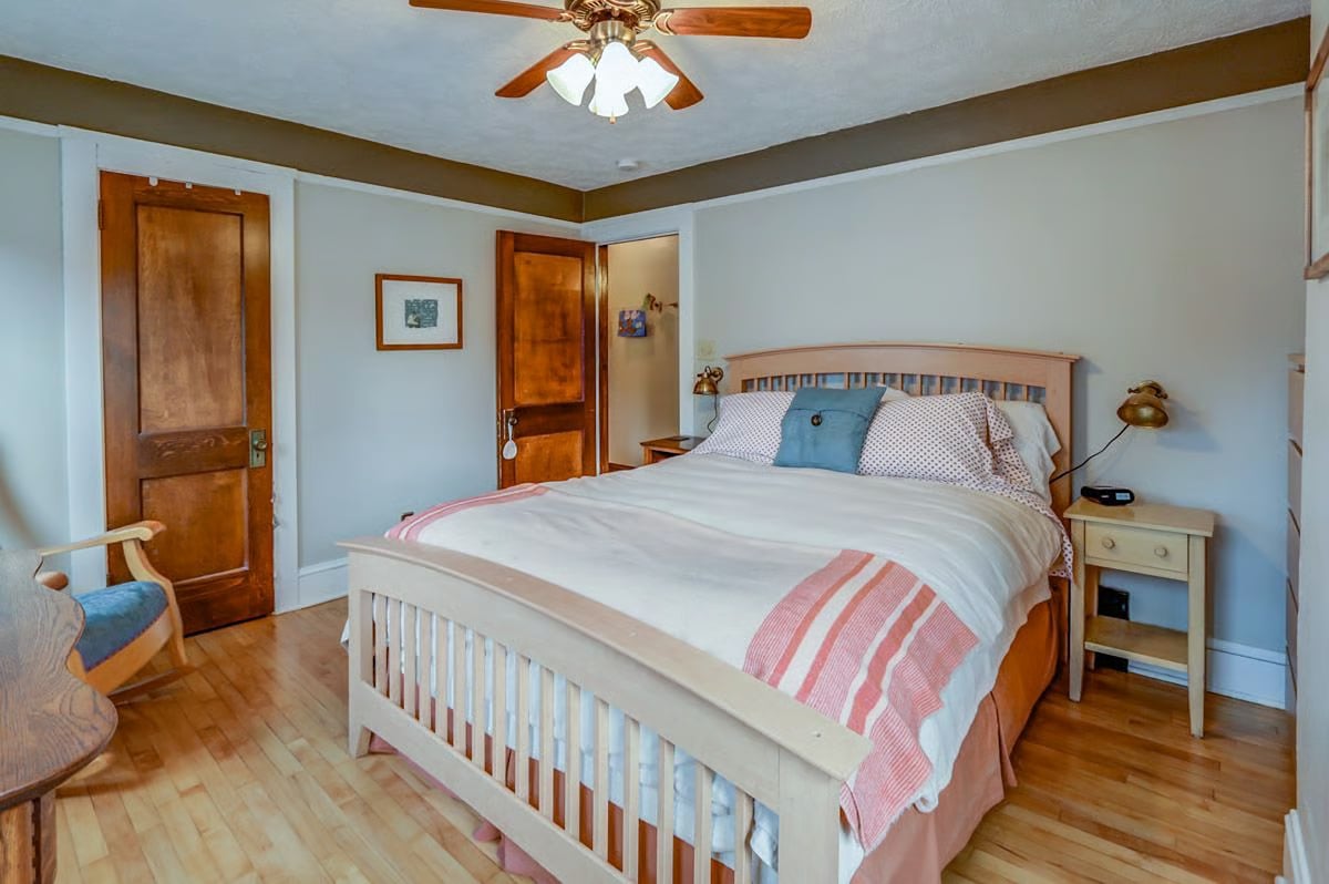 Bedroom with a light-wood bed, coral-striped bedding, hardwood floors, and a ceiling fan.