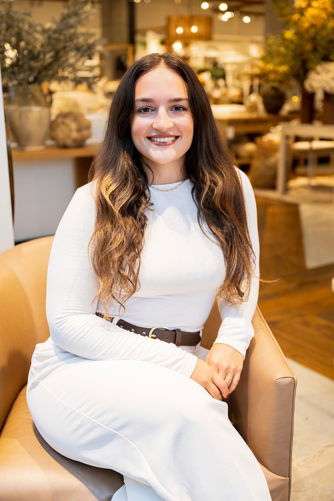 Konstantina Colebrook seated in a tan armchair, wearing a white dress.