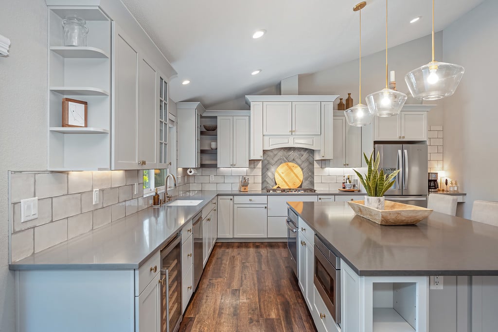 Bright kitchen with white cabinets, gray island, pendant lights, and stainless steel appliances.