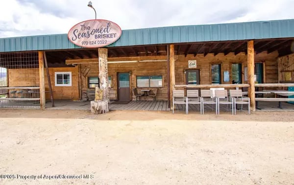 Rustic wood restaurant with a blue roof, covered porch, and outdoor seating beneath a “The Seasoned Brisket” sign.