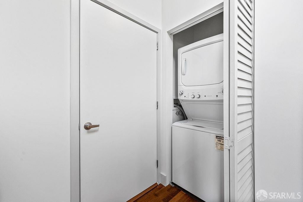 Laundry closet with a stacked white washer and dryer behind an open louvered door.
