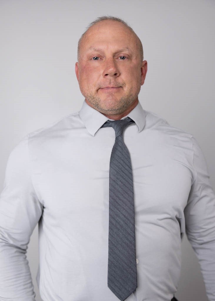 Sam Bingham in a white shirt and gray tie against a plain light background.