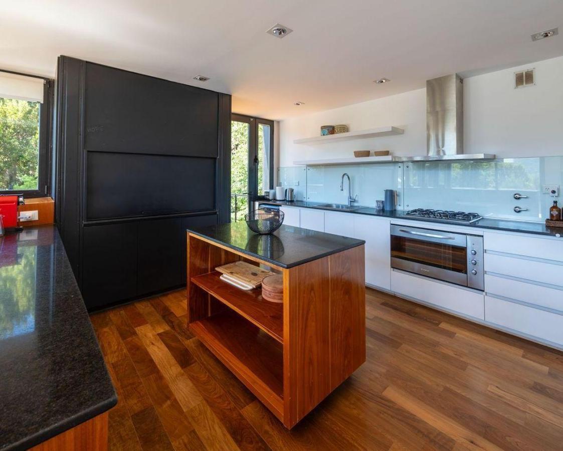 Modern kitchen with a wood-sided island, dark stone counters, and windows overlooking greenery.