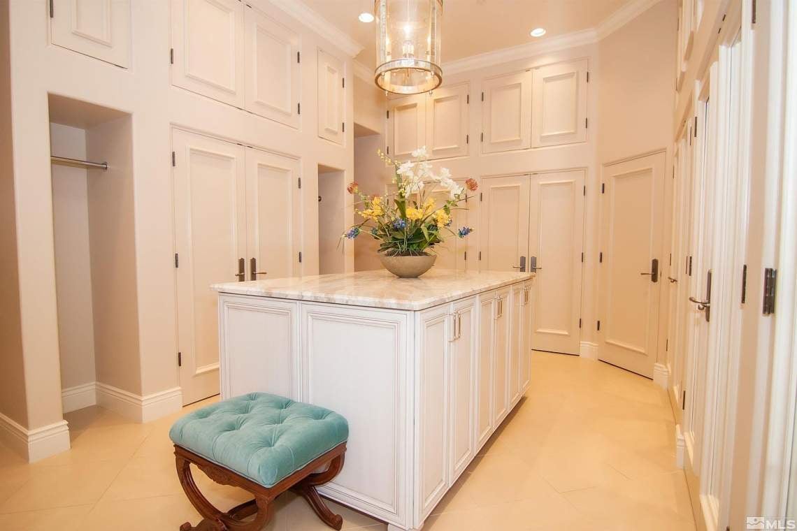 Walk-in dressing room with a marble-top island, white cabinetry, and a teal upholstered stool.