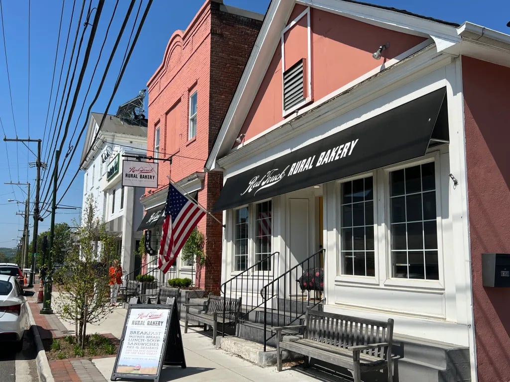 Red Truck Rural Bakery storefront in Marshall, Virginia with a black awning, American flag and sidewalk benches along Main Street