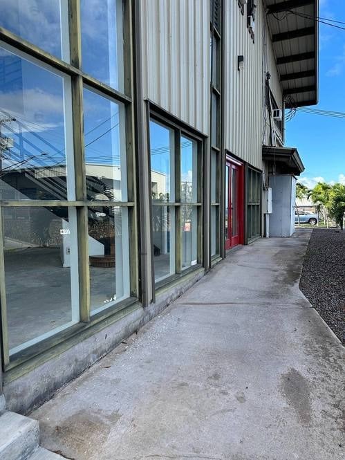 Commercial building with tall glass storefront windows, a red entrance door, and a concrete walkway.