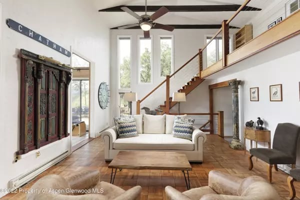 Double-height living room with a white sofa, parquet flooring, and an open staircase to a loft.
