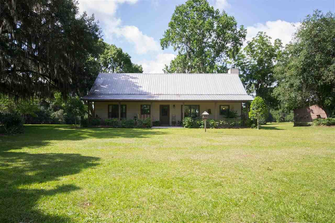 A serene home surrounded by a lush field, dotted with trees and vibrant green grass under a clear sky.