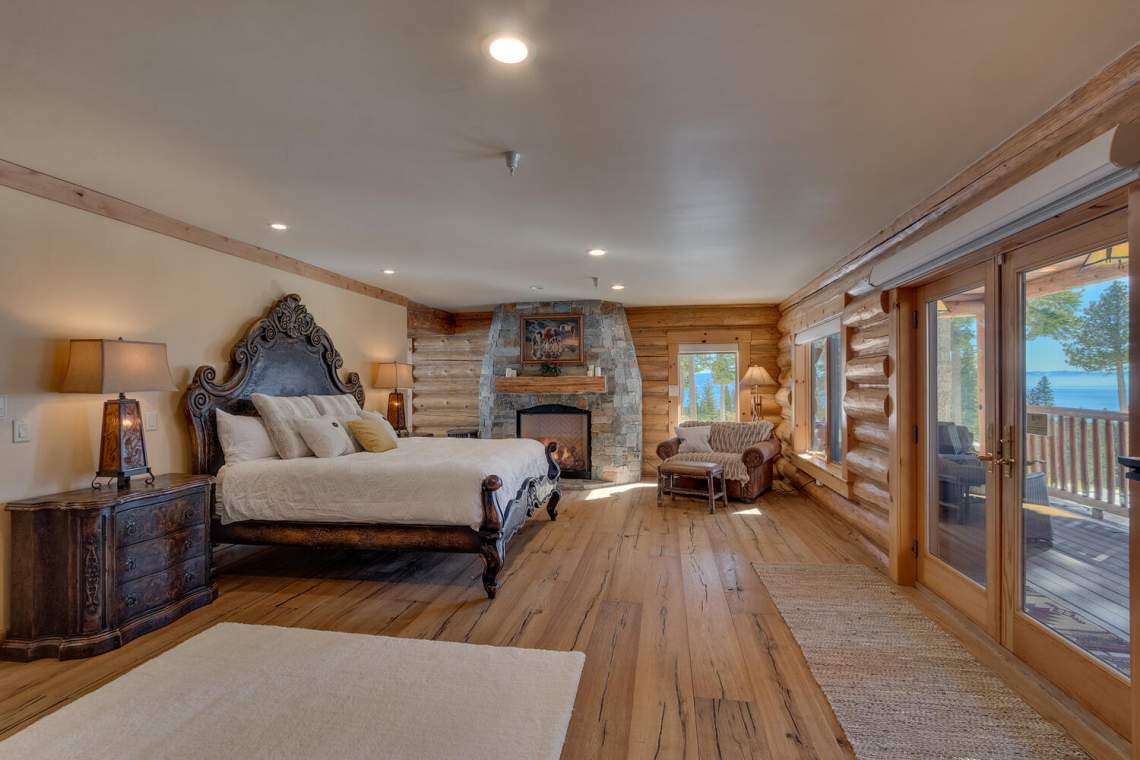 Log-cabin bedroom with a stone fireplace and lake view through glass doors.