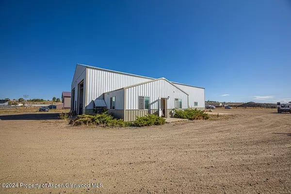 Metal-sided commercial building beside a wide gravel lot under a clear blue sky.