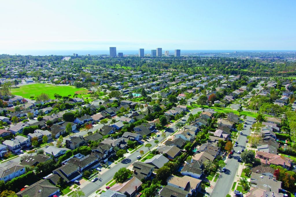 Tree-lined cul-de-sac street in the Port Streets neighborhood beside a hillside view of Eastbluff homes overlooking Newport Beach's Back Bay