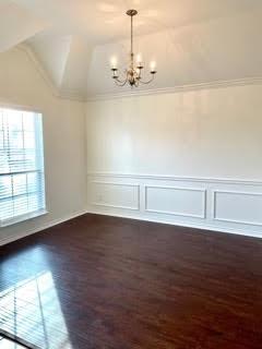 Empty dining room with dark hardwood floors, white wainscoting, and a chandelier.