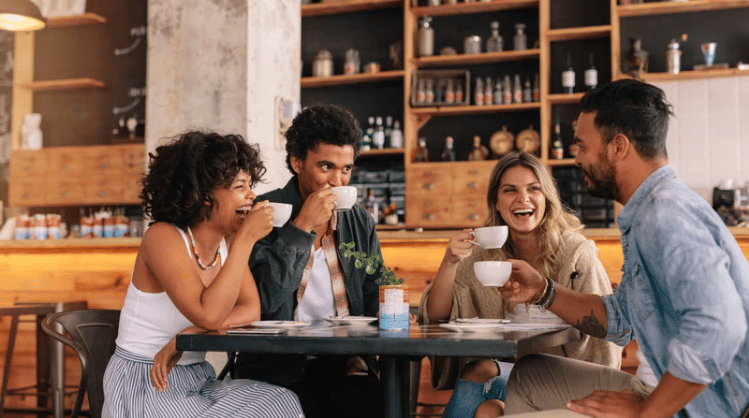 Four friends laugh and talk over coffee at a café table.