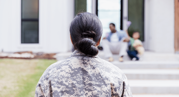 Female U.S. military veteran in uniform facing her family on the front steps of their home, symbolizing VA loan homeownership benefits.