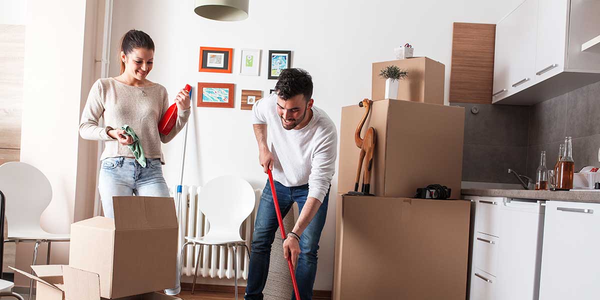 A couple cleans a kitchen while unpacking boxes in their new home.