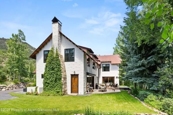 White multi-level home with a tall stone chimney, ivy-covered wall, and landscaped lawn.