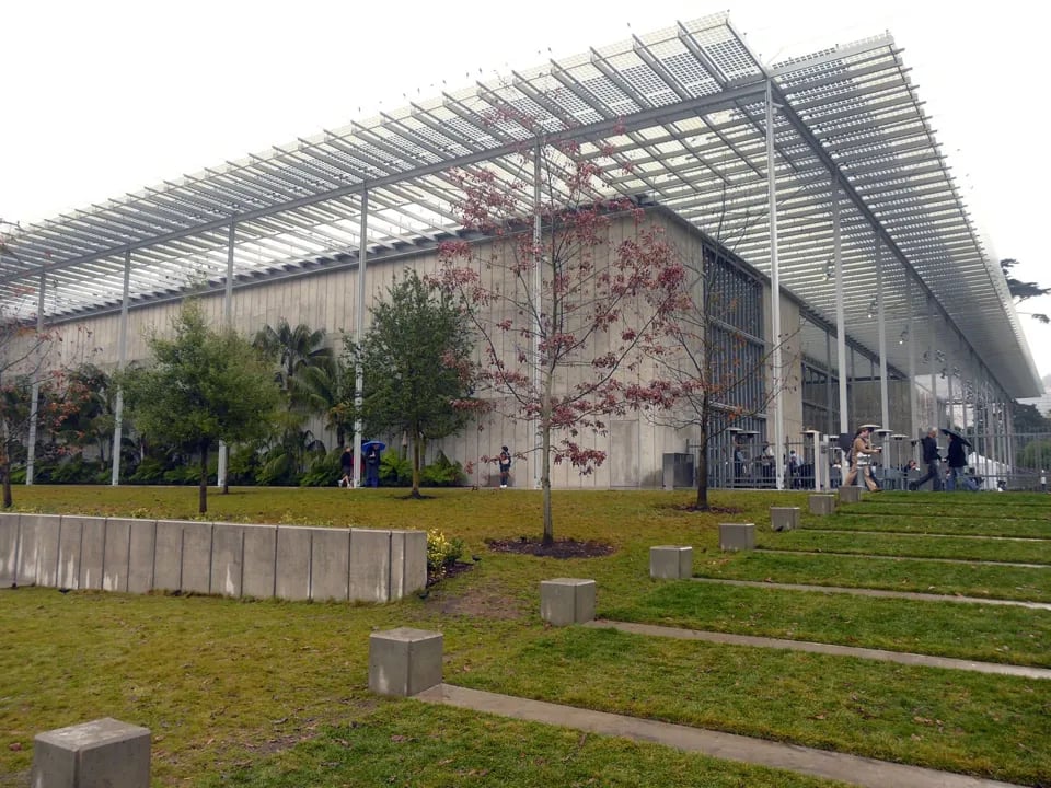 Exterior view of California Academy of Sciences showing concrete walls, solar panel canopy, and trees.
