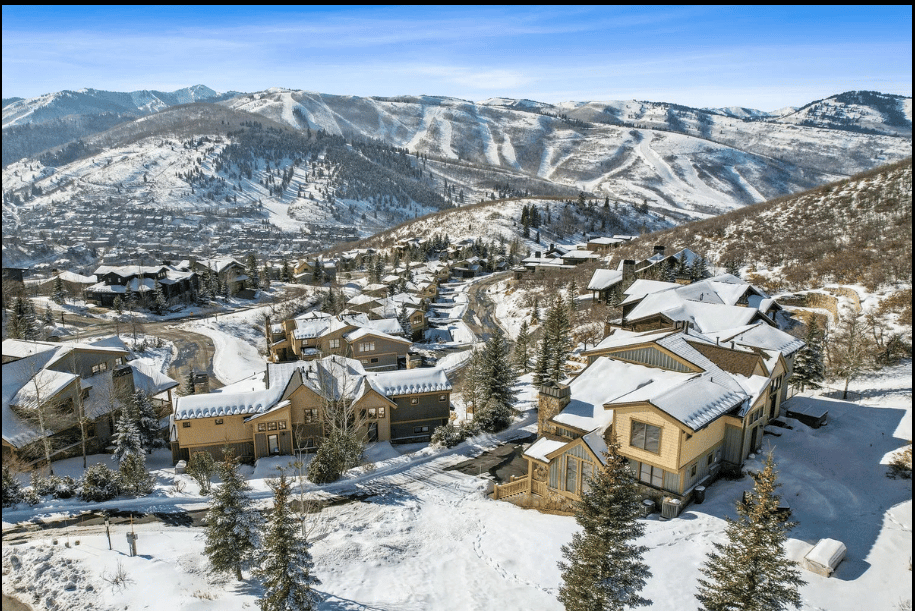 Aerial view of snow-covered homes with mountain ski slopes in the background.