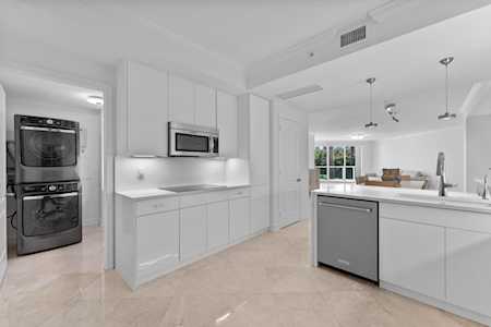 Modern white kitchen with double wall ovens and a large island opening to a bright living area.