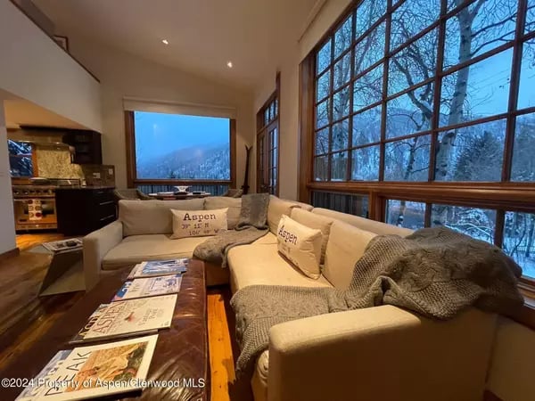 Aspen living room with cream sectional sofas and tall windows overlooking snowy trees and mountains.
