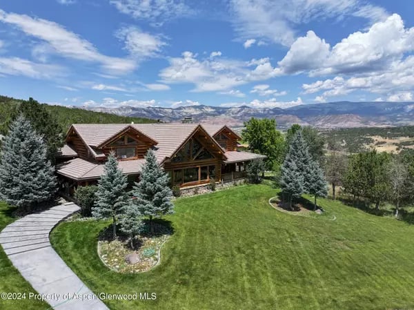 Log-style home with timber gables and a curved walkway, surrounded by evergreens with mountain views.
