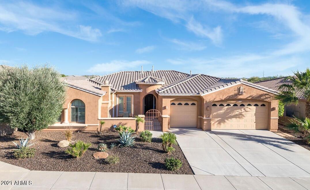 Peach stucco home with a tiled roof, arched entry, two garage doors, and desert landscaping.