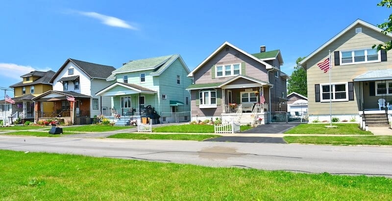 Colorful detached homes with front lawns and American flags along a residential street.