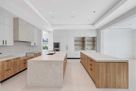 Modern kitchen with a large pale stone island, white cabinetry, and warm wood lower cabinets.