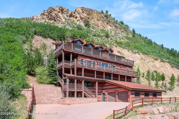Multistory timber home with wraparound decks on a rocky, wooded hillside.