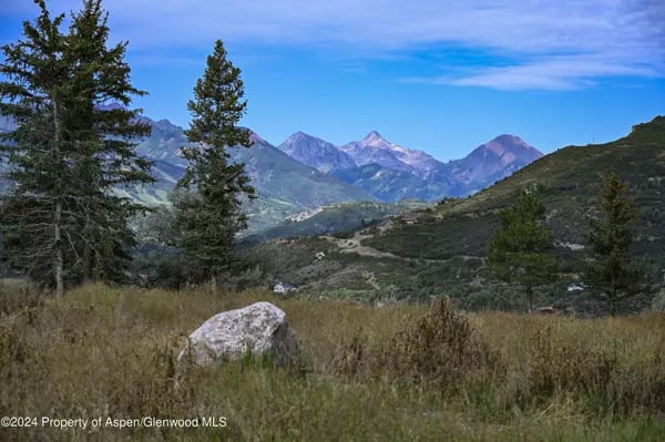 Mountain range near Aspen beyond grassy hills and evergreen trees.