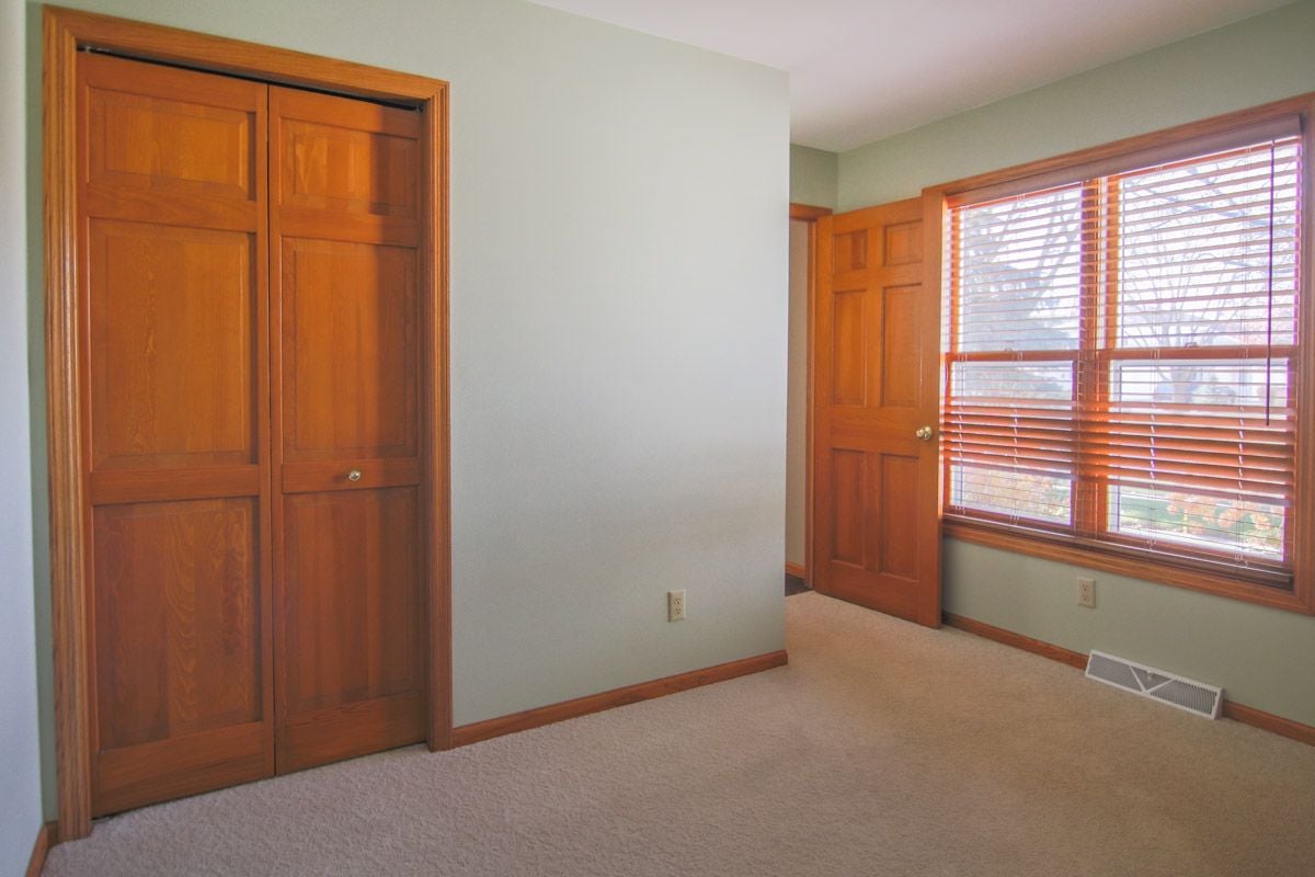 Empty room with a large wooden closet and wide window with wooden blinds.