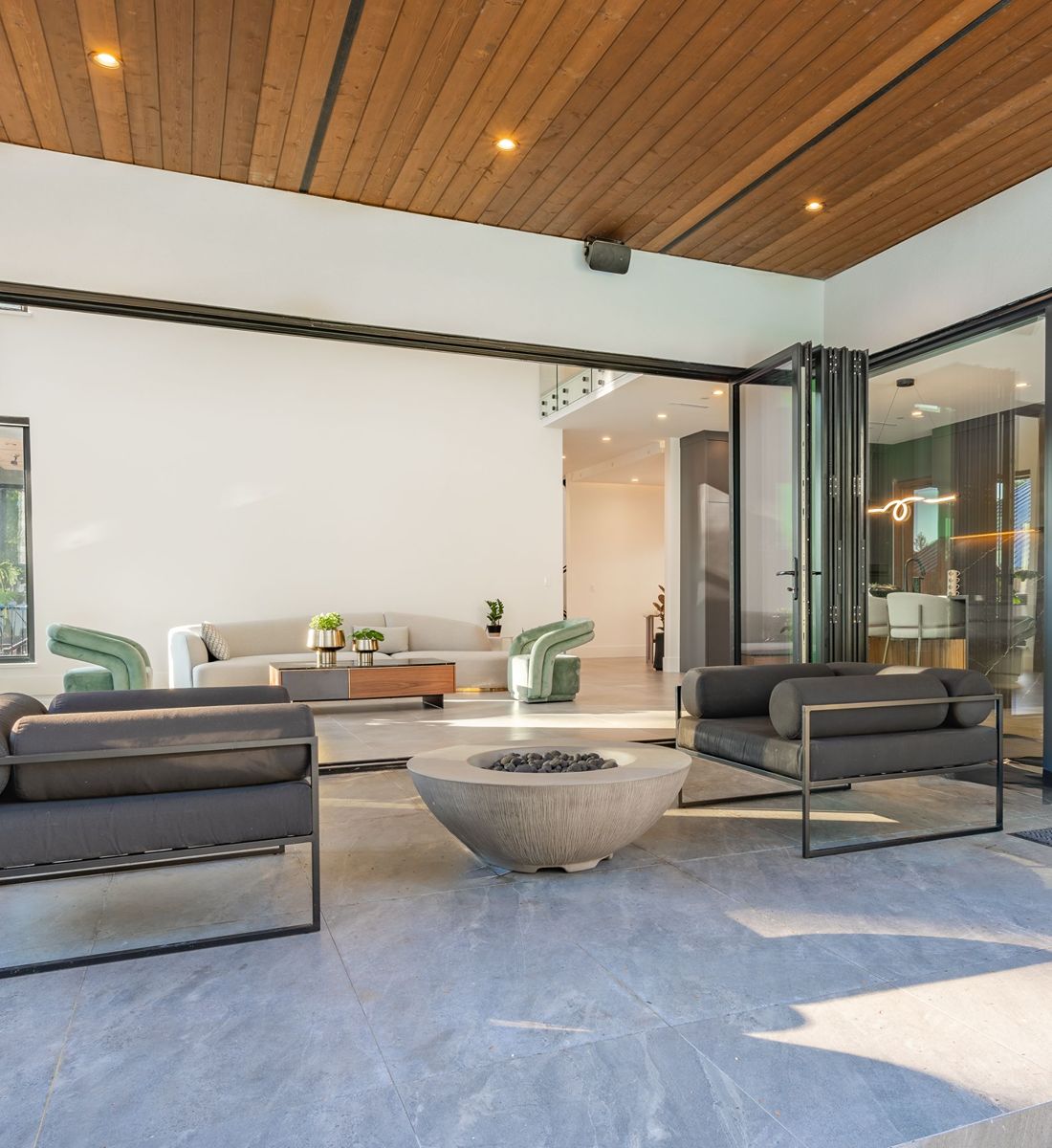 Modern living room with a wood-plank ceiling, sculptural seating, and folding glass doors.