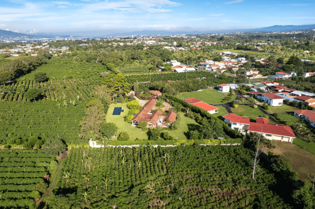 Aerial view of a red-tile hacienda estate with a pool, surrounded by greenery and distant mountain ridges.