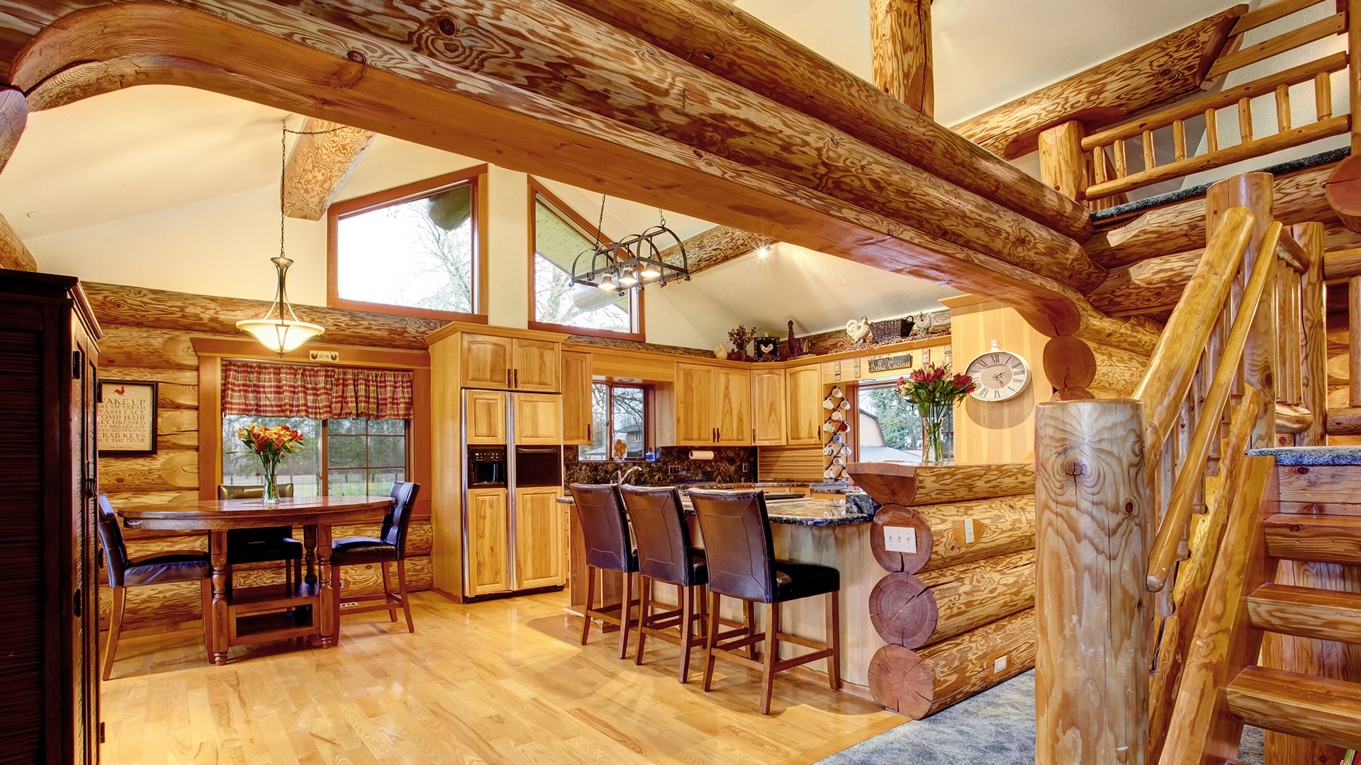 Log-cabin kitchen with exposed timber beams, a granite island, bar stools, and a dining table.