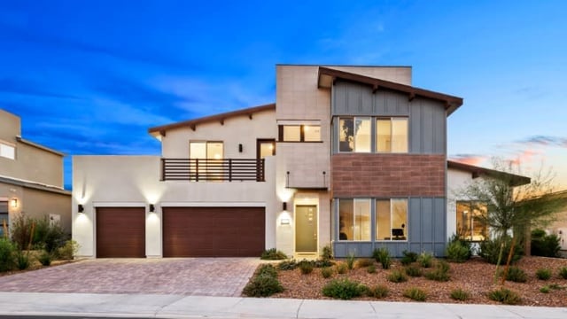 Modern two-story home with a stone facade, balcony, and double garage at dusk.