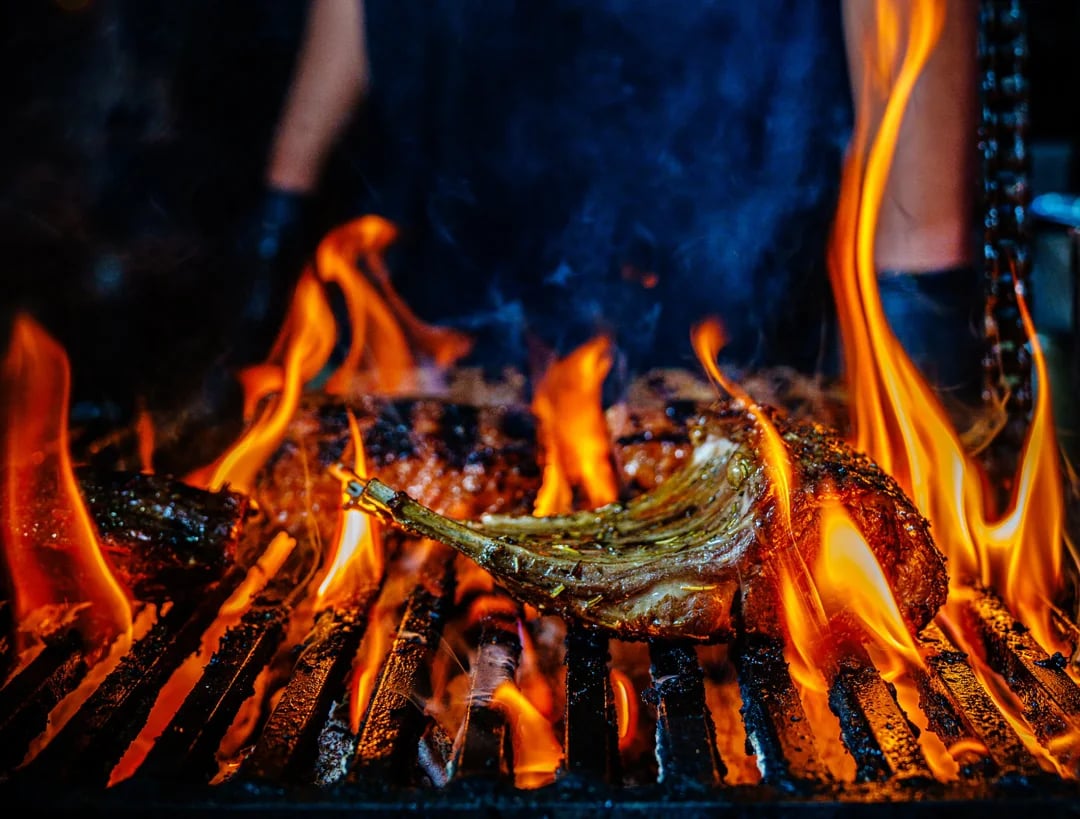 Bone-in steak grilling over flames on a barbecue.
