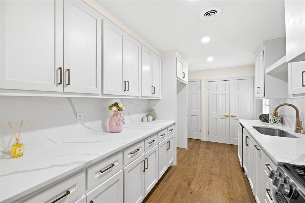 Bright white galley kitchen with veined counters, brass hardware, and warm wood floors.