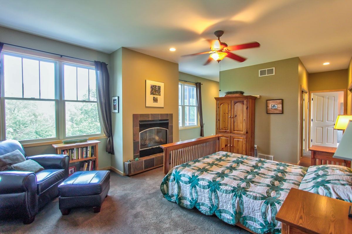 Bedroom with a fireplace, large windows, wooden armoire, and patterned quilt.