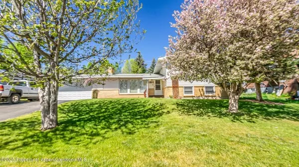 Single-story ranch home behind a broad green lawn, with flowering trees and a driveway.