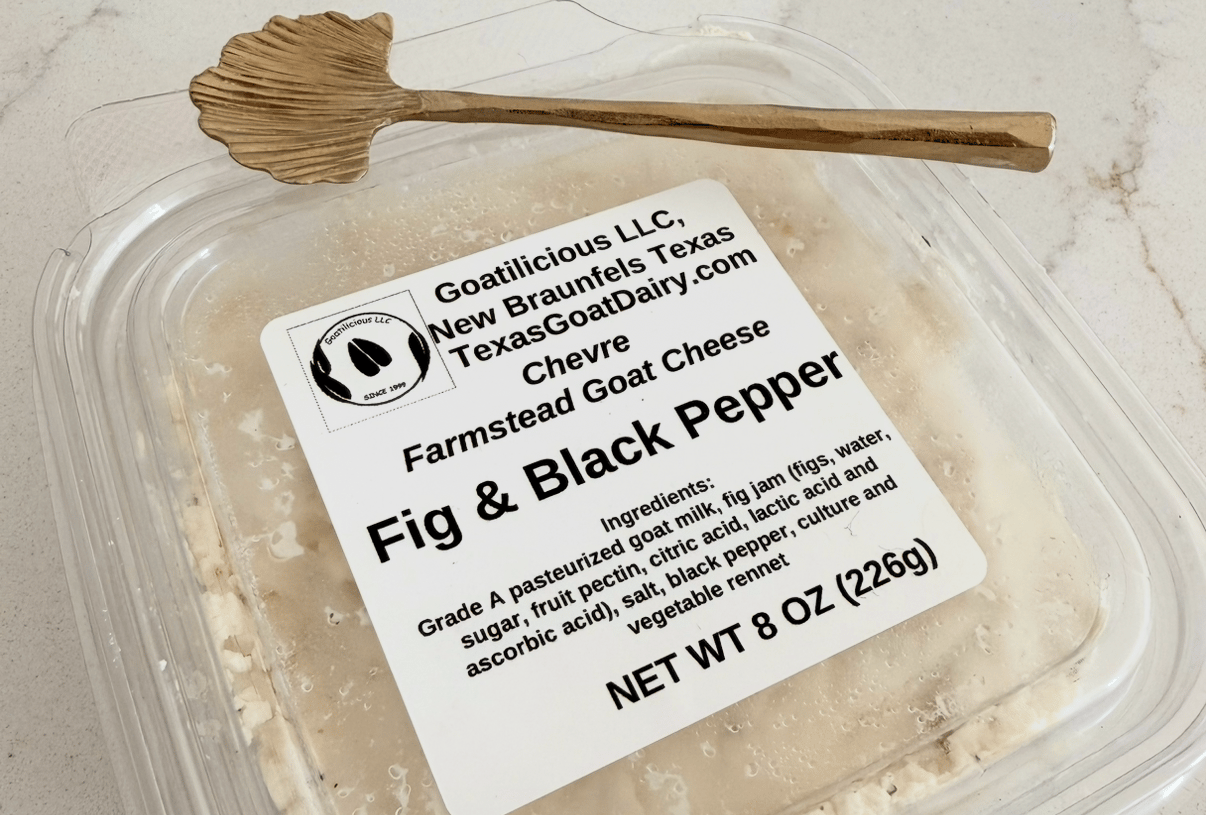 Fig and black pepper chèvre in a clear container with a wooden spreader.