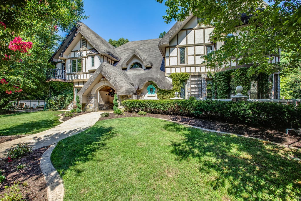 Whimsical Tudor-style house with steep shingle roofs, ivy-covered walls, and a curved walkway.