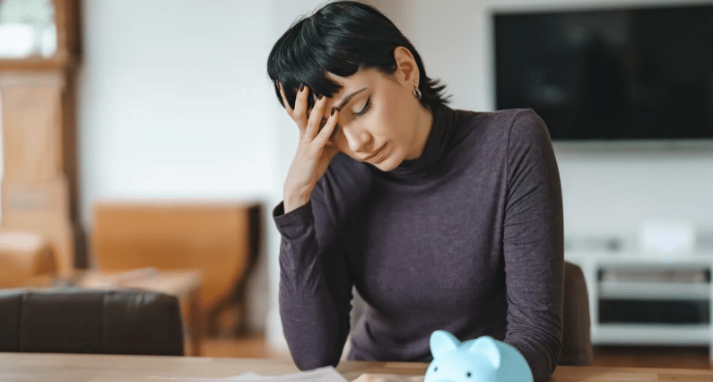 Woman reviews paperwork beside a blue piggy bank, looking worried.