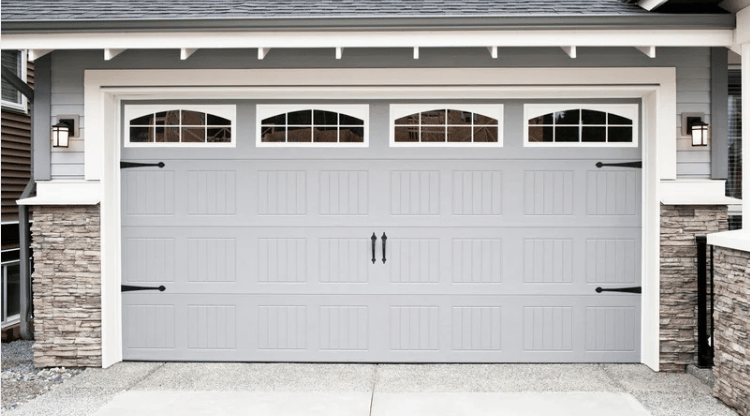 White double garage door with arched windows and black hardware on a gray house with stone accents.