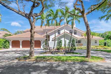 White home with arched garage doors, a tile roof, and mature trees along the driveway.